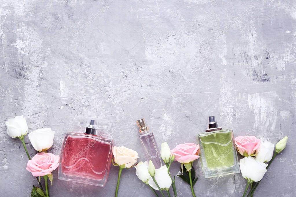 Perfume bottles with flowers on grey wooden table