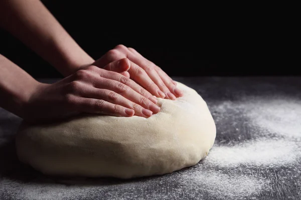 female hands knead dough on black wooden table