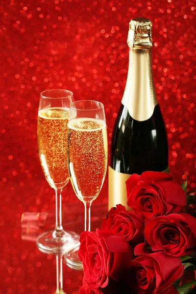 Champagne bottle with glasses and bouquet of red roses on lights background