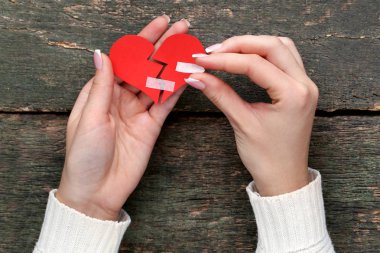 Yapışkanlı bandaj ile kırmızı kağıt kalp tutan eller