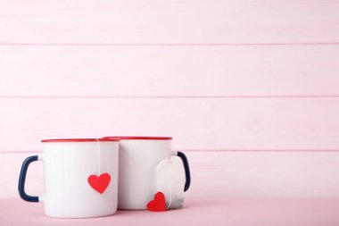Kırmızı Kalpler ve pembe bir arka plan üzerinde çay poşeti ile çay kupaları