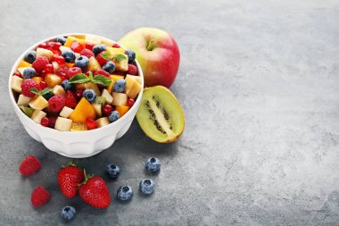 Gri ahşap masa üzerinde kase taze meyve salatası