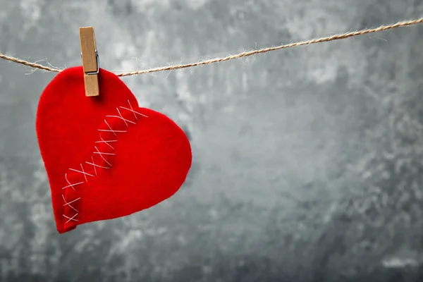 Broken red heart hanging on rope on grey background