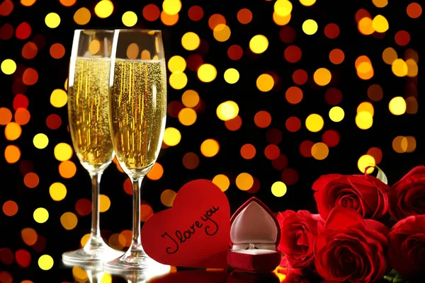 Champagne glasses with red roses and silver ring on lights background