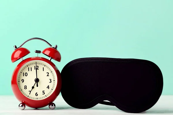 Red alarm clock with sleeping mask on mint background