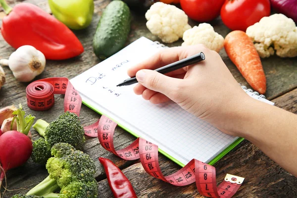 女性手写膳食菜单纸上的蔬菜在木桌上 — 图库照片