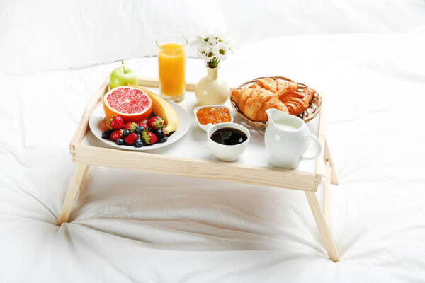 Tasty breakfast in bed on wooden tray