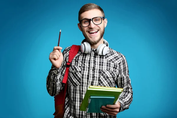 Young man with backpack, headphones and notebooks on blue background