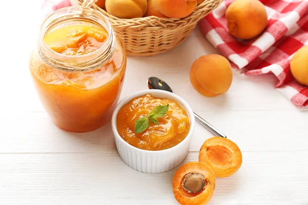 Beyaz ahşap masa üzerinde kase ve cam kavanoza kayısı reçeli