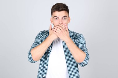 Genç adam gri arka planda elleri ile ağzını kapatıyor.