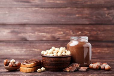 Erimiş çikolatalı ekmek ve kahverengi ahşap üzerinde soyulmuş fındık.