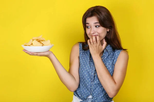 Junge Frau mit Kartoffelchips im Teller auf gelbem Hintergrund — Stockfoto