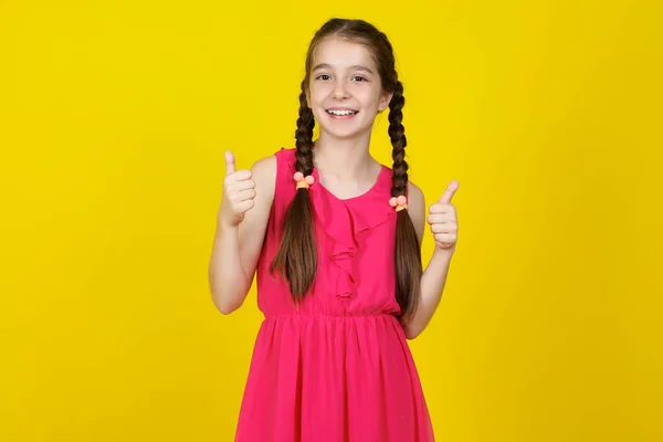 Hermosa joven en vestido rosa mostrando los pulgares hacia arriba en amarillo b — Foto de Stock
