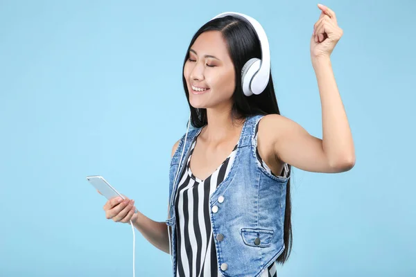 Krásná žena se sluchátky a smartphone na modrém pozadí — Stock fotografie