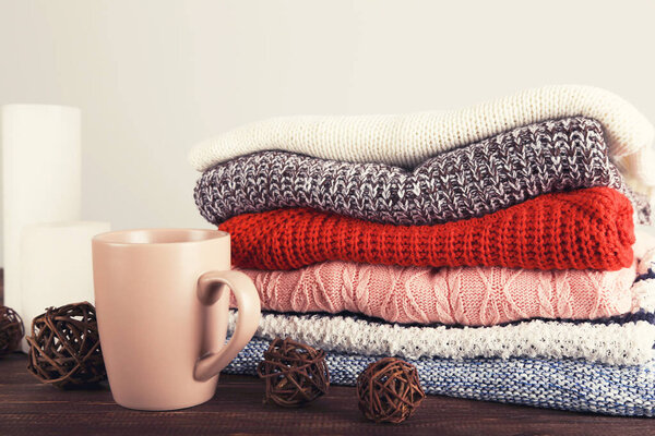 Folded knitted sweaters with cup of tea on grey background