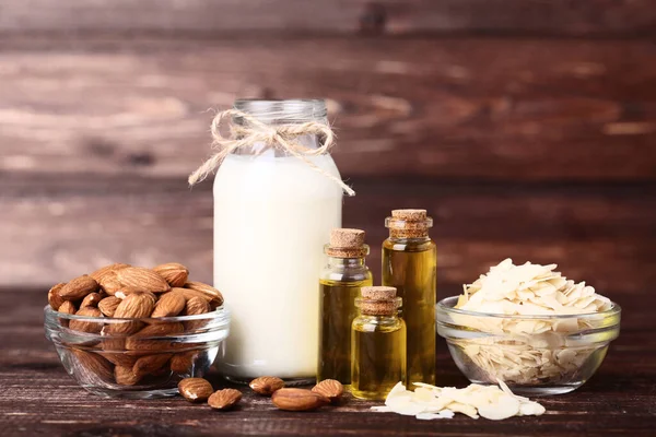 Mandeln mit Öl und Milch in Flaschen auf braunem Holztisch — Stockfoto