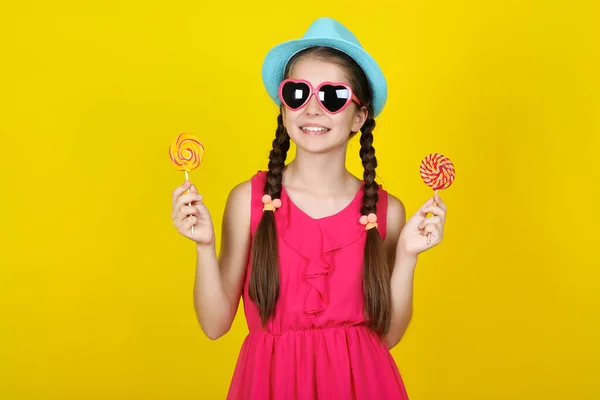 Schöne junge Mädchen mit süßen Lutschern auf gelbem Hintergrund — Stockfoto