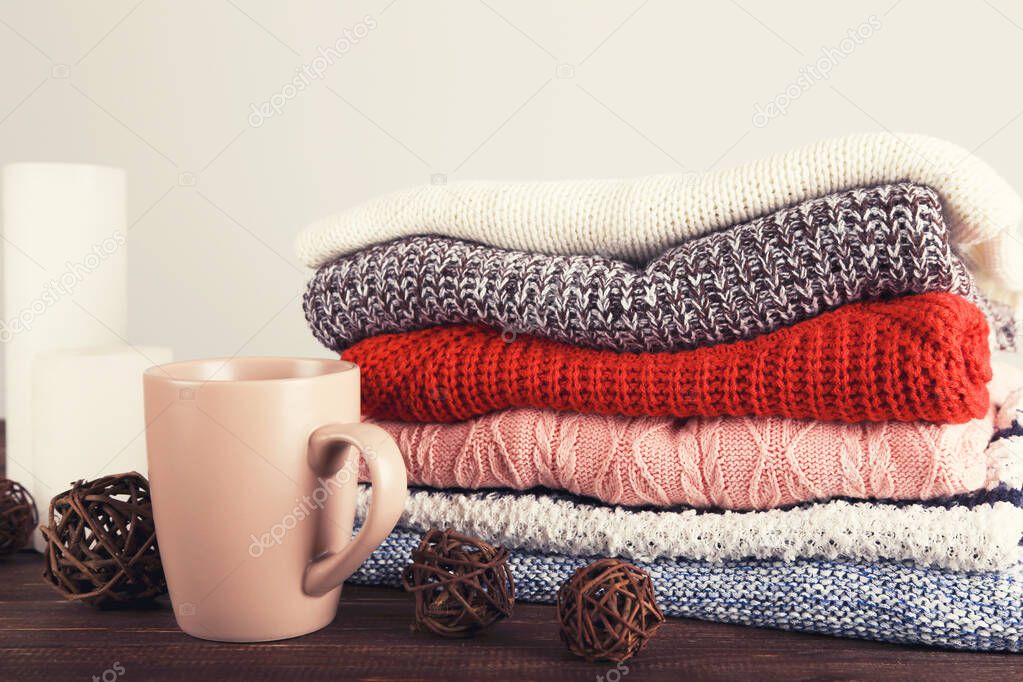 Folded knitted sweaters with cup of tea on grey background