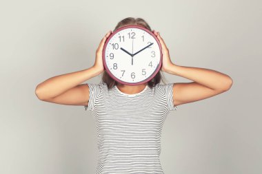 Genç kız, gri arka planda saat yuvarlak yüzünü kapatıyor