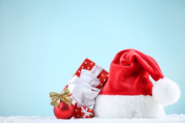 Kırmızı Noel Baba şapkası ve mavi arka planda hediye kutuları.