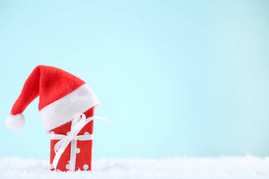 Mavi arka planda hediye kutusu olan kırmızı Noel Baba şapkası.