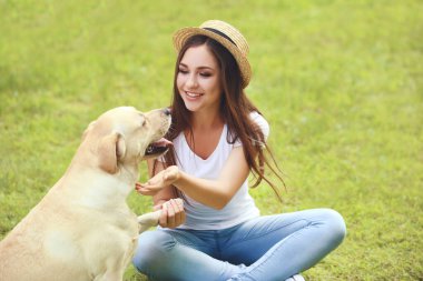 Şapkalı genç kız parkta oturmuş köpeği okşuyor.