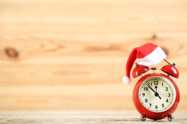 Kahverengi ahşap arka planda Noel Baba şapkası olan kırmızı alarm saati.