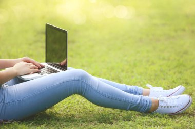 Dizüstü bilgisayarı olan genç bir kız parkta çimlerde oturuyor.