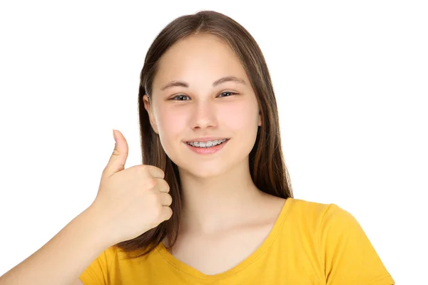 Dişlerinde diş teli olan genç bir kız beyaz sırtında baş parmağını gösteriyor. — Stok fotoğraf