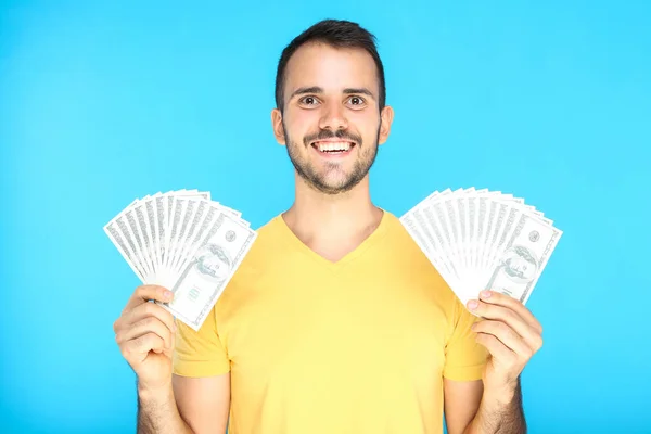 Joven hombre feliz sosteniendo billetes de dólar sobre fondo azul — Foto de Stock