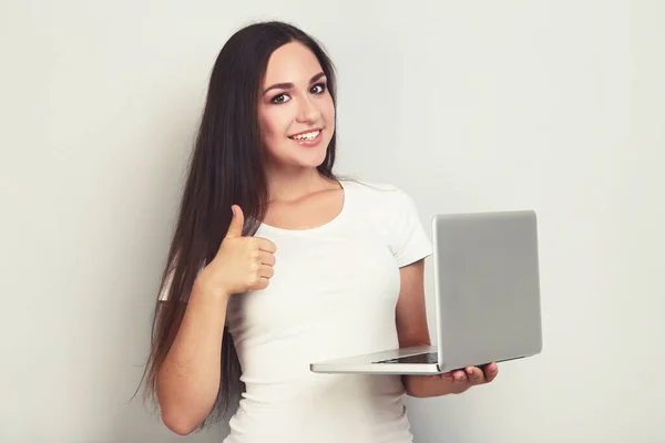 Молодая девушка с ноутбуком показывает большой палец вверх на серой backgro — стоковое фото