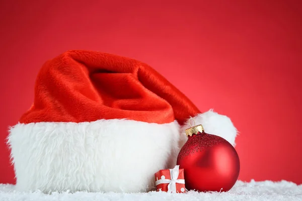 Chapeau santa rouge avec boule et boîte cadeau sur fond rouge — Photo