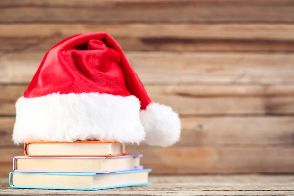 Sombrero rojo de santa con pila de libros sobre fondo marrón de madera — Foto de Stock