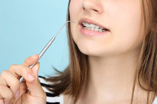 Menina com aparelho dentário segurando ferramenta dentista em azul backg — Fotografia de Stock