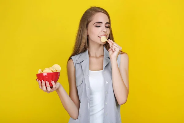 Молодая красивая девушка ест чипсы на желтом фоне — стоковое фото
