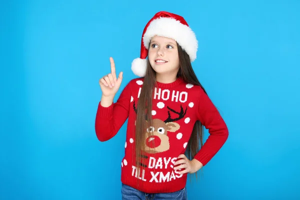 크리스마스 스웨터를 입고 모자를 쓰고 파란 배경에 손가락을 보이는 소녀 — 스톡 사진