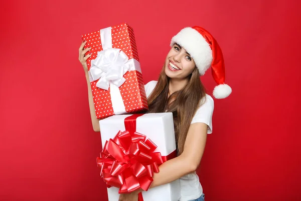 Bella donna che indossa il cappello di Babbo Natale e che tiene scatole regalo sul rosso — Foto Stock