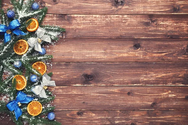 Kerstboomtakken met speelgoed en sinaasappelfruit op bruin hout — Stockfoto