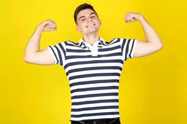 Młody mężczyzna pokazuje mięśnie dłoni na żółtym tle — Zdjęcie stockowe