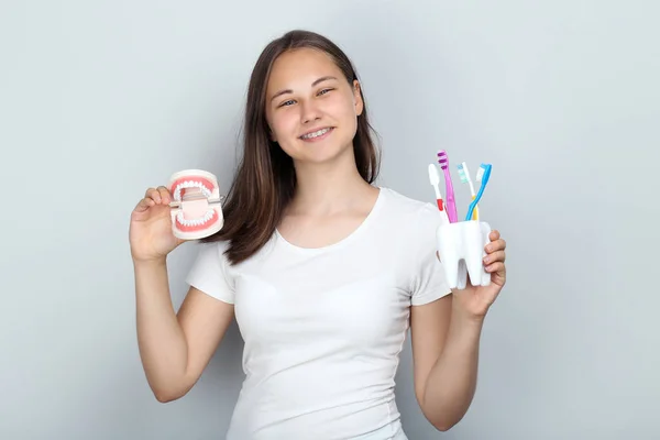 Молода дівчина з зубними брекетами тримає модель зубів і зубну щітку — стокове фото