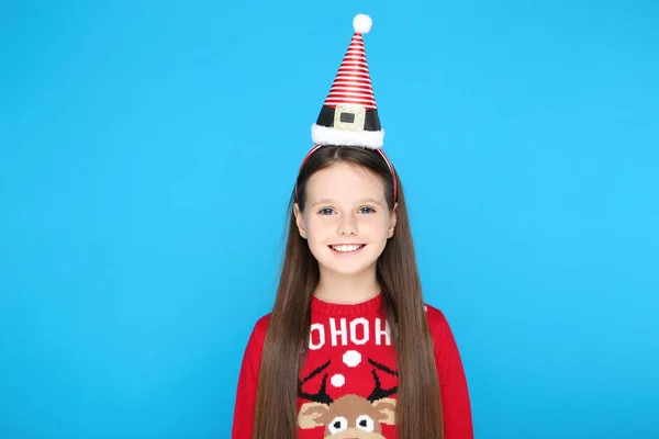 Liten flicka i tröja och jul mössa på blå bakgrund — Stockfoto