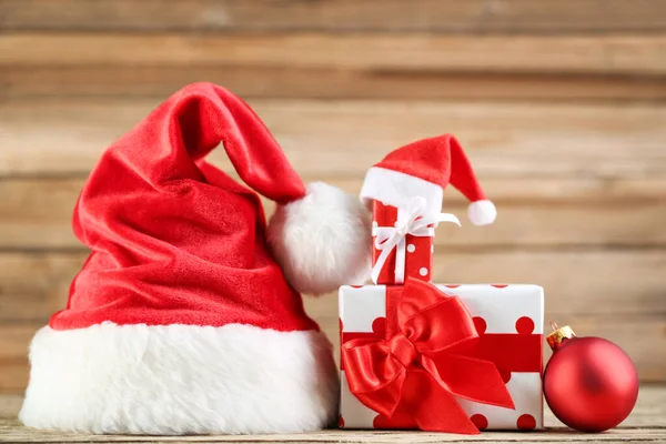 Chapeaux de Père Noël rouge avec boîtes-cadeaux et boule sur backgr en bois brun — Photo