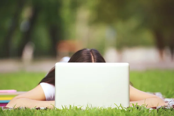 Молода дівчина з ноутбуком лежить на траві в парку — стокове фото