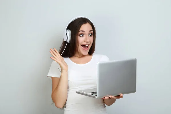 Młoda dziewczyna w słuchawkach z laptopem na szarym tle — Zdjęcie stockowe
