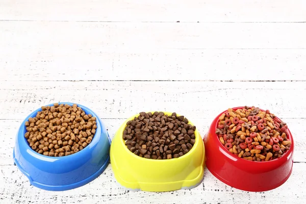 Dry pet food in bowls on white wooden table