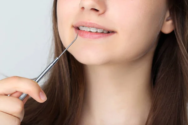 Jovem com aparelho dentário segurando ferramenta de dentista em cinza backg — Fotografia de Stock