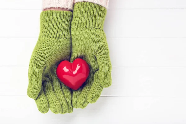Händerna i stickade vantar håller hjärtat på vitt träbord — Stockfoto
