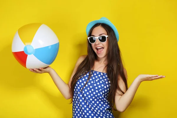 Junges Mädchen mit Sonnenbrille mit aufblasbarem Ball auf gelbem Hintergrund — Stockfoto