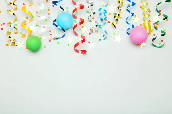 Fitas coloridas com balões de borracha e confete em cinza backgr — Fotografia de Stock
