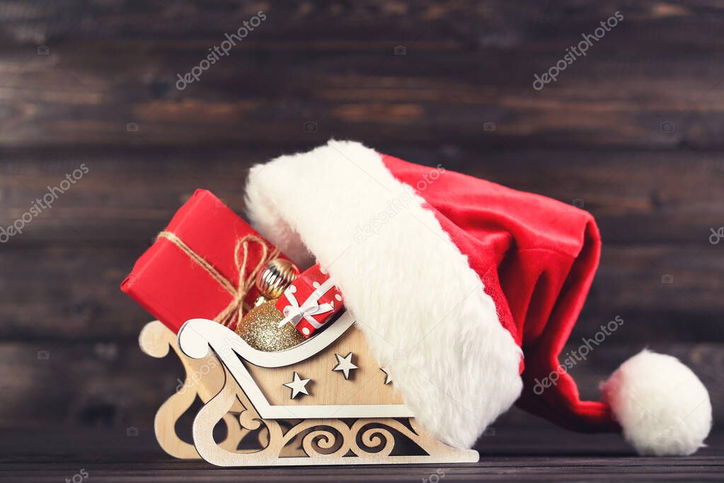 Red santa hat with gift boxes, baubles and sleigh on brown woode